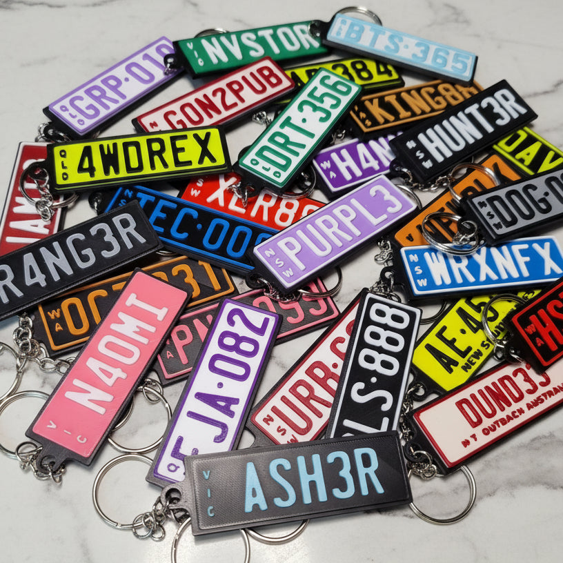 A pile of colorful novelty license plate keychains with metal key rings, arranged on a marble surface.