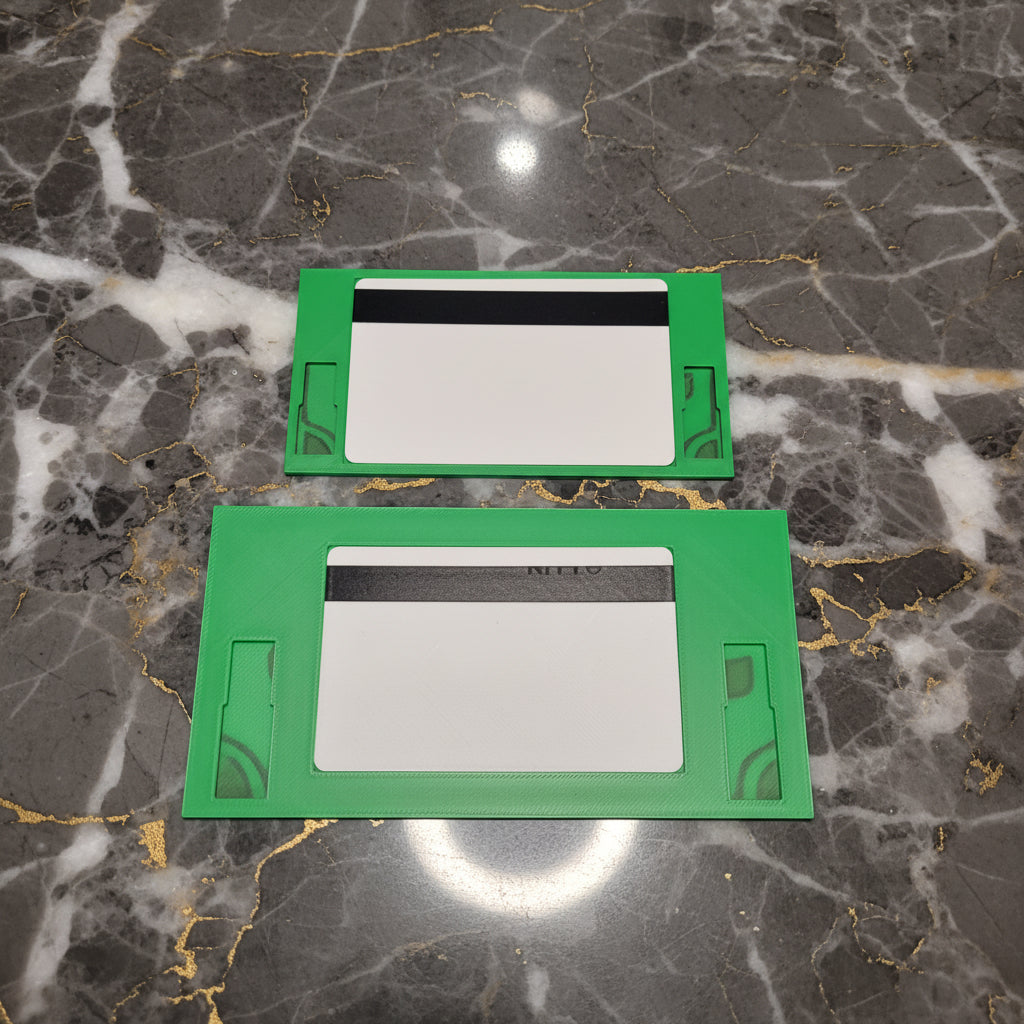 Two green rectangular plastic trim pieces or cover plates with cutouts, displayed against a marble background.